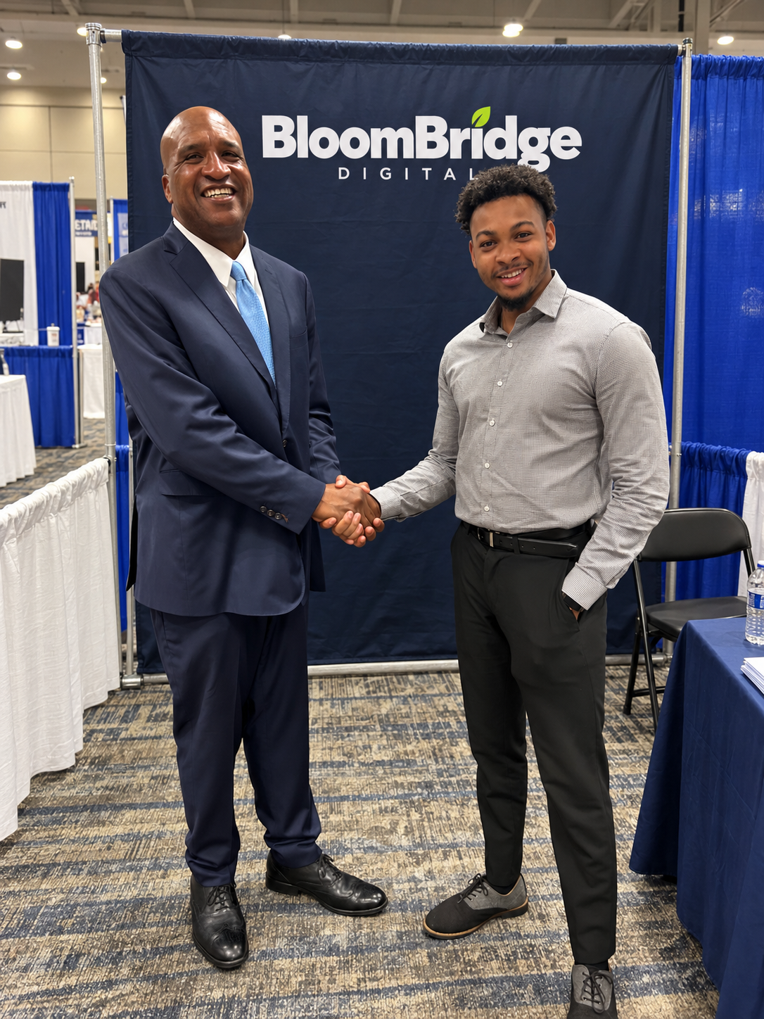 Kenneth Foxworth of BloomBridge Digital shaking hands with a guest in front of the BloomBridge Digital booth banner